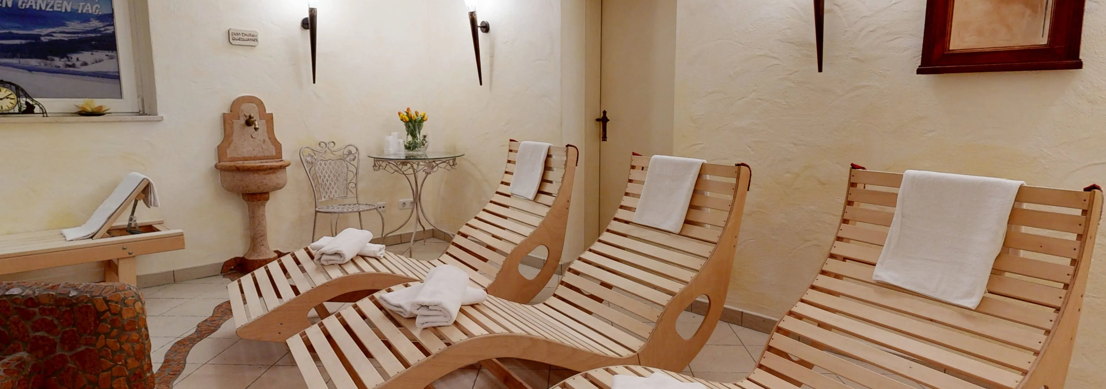 Holzliegestühle mit Handtüchern in einem Wellnessbereich, dekoriert mit Pflanzen.