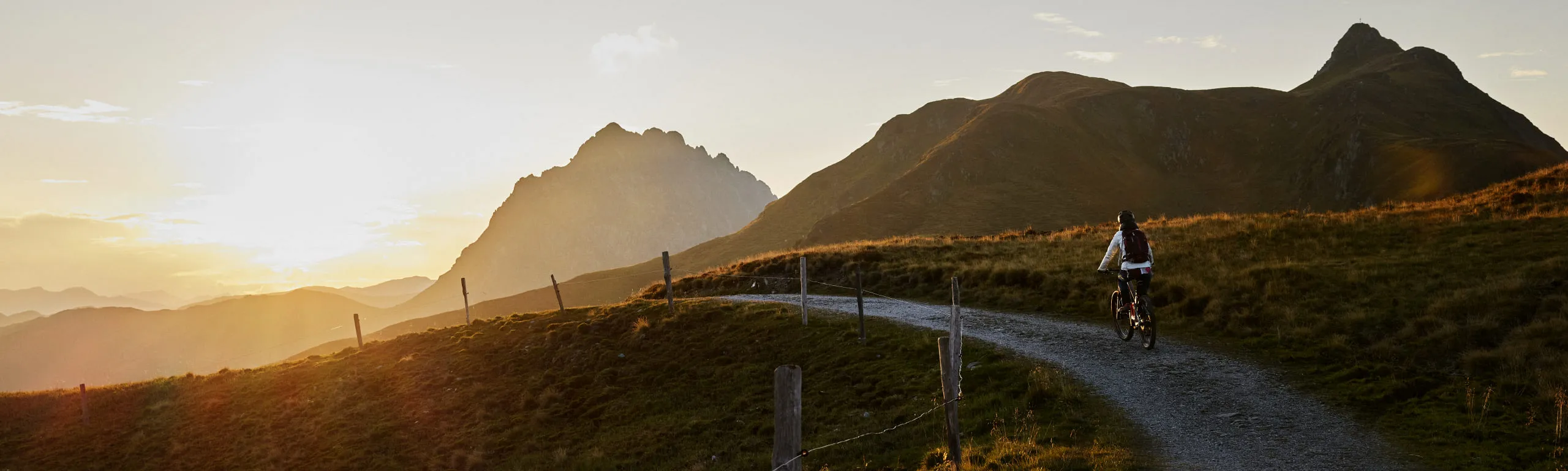 Radfahrer auf einem Weg mit Bergen und Sonnenuntergang im Hintergrund