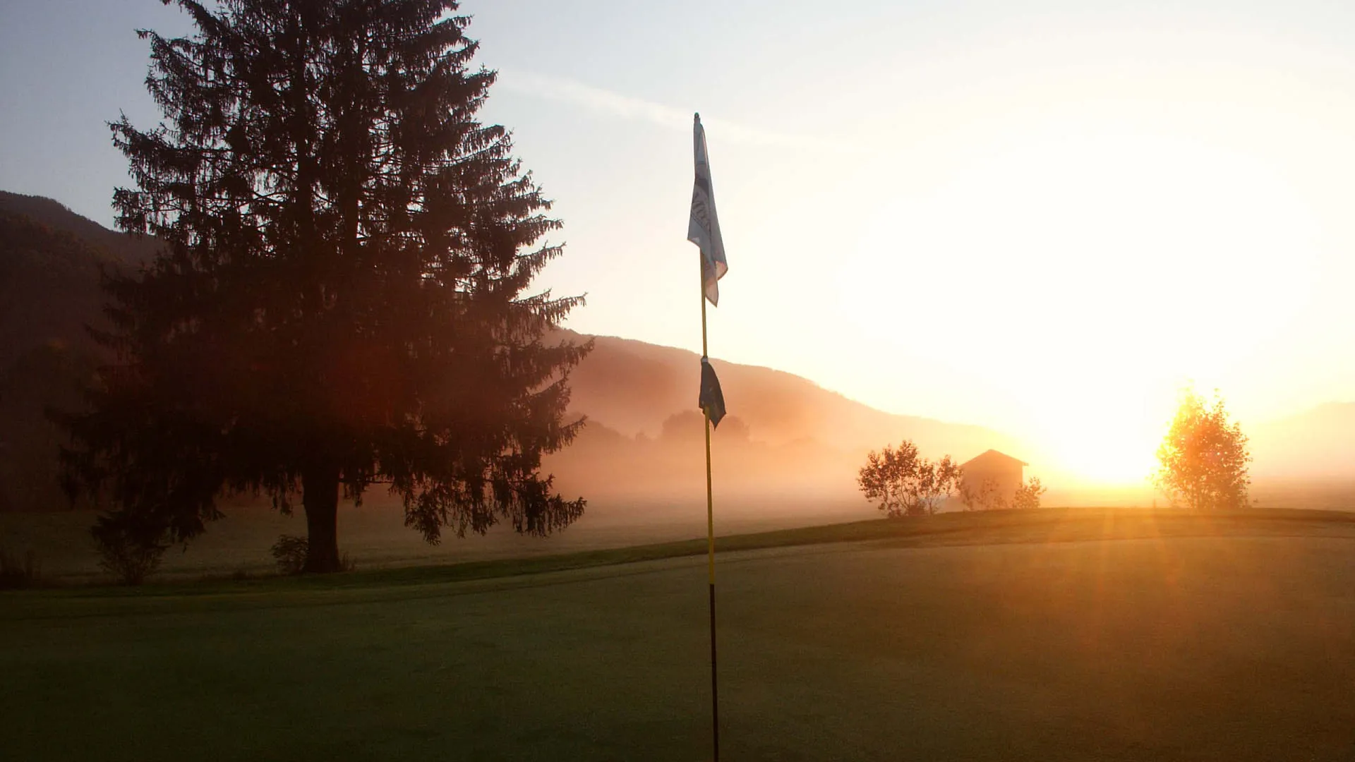 Golfplatz Hohe Tauern bei Sonnenaufgang mit Fahne und Baum im Vordergrund