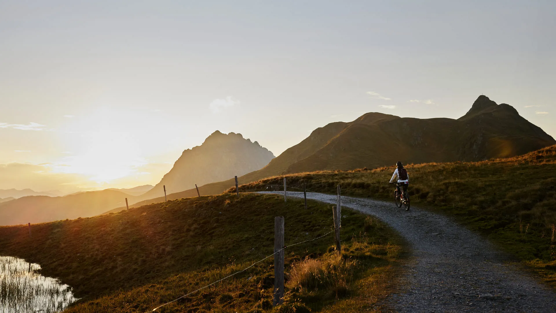 Sonnenuntergang über einem berghang mit Radfahrer auf einem Schotterweg.