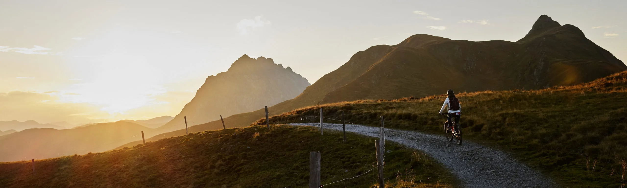 Radfahrer auf einem Weg in den Bergen bei Sonnenuntergang.