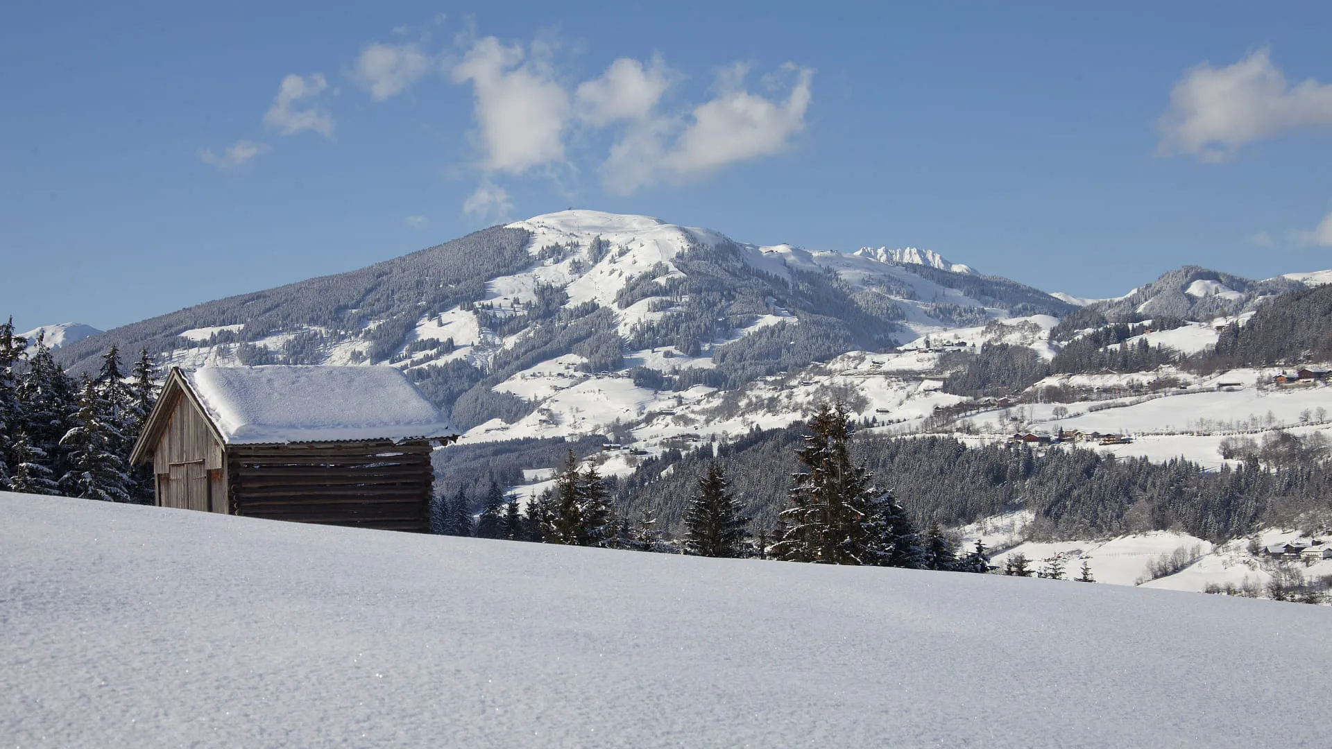 Schneebedeckter Hügel mit einem kleinen Holzhaus im Vordergrund