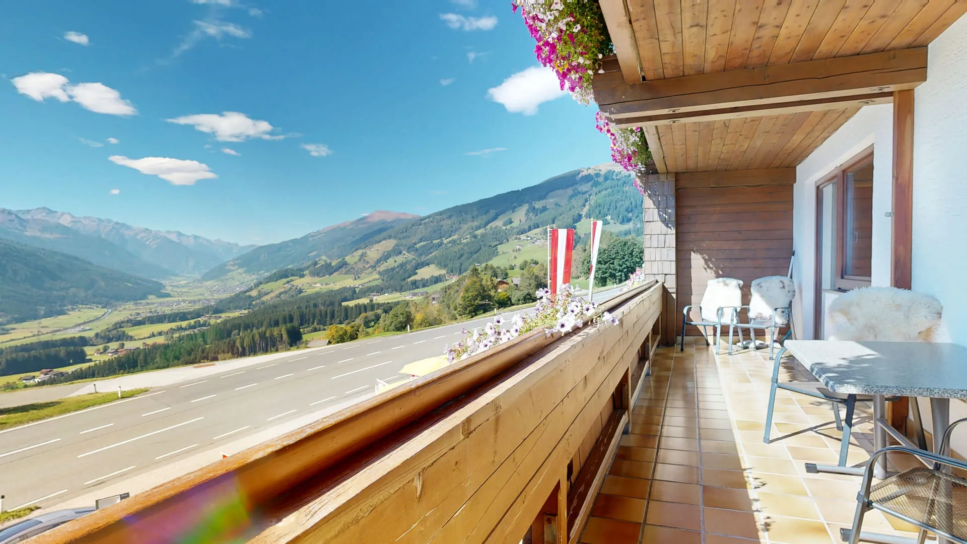 Bergpanorama mit Blick auf bewaldete Hügel und blauen Himmel, Terrasse im Vordergrund.