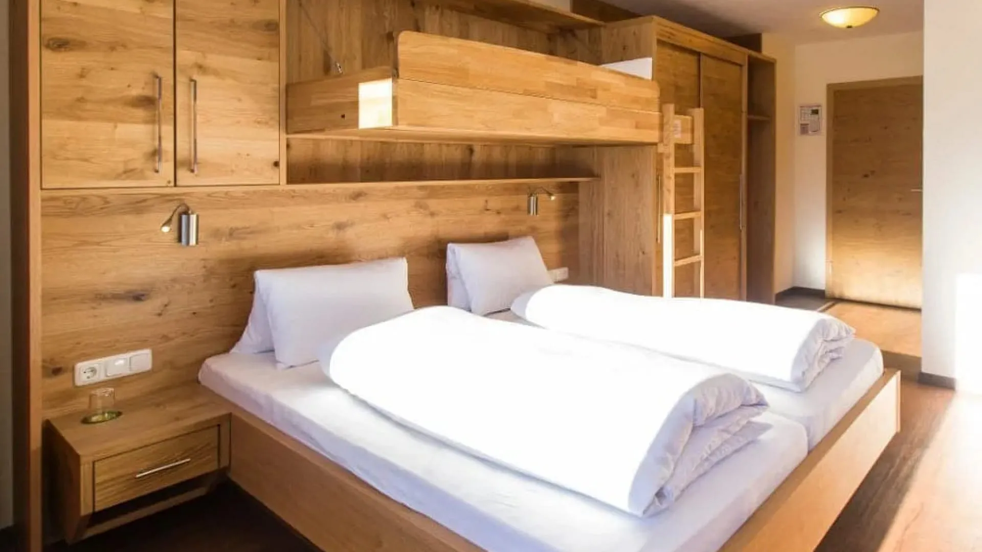 Helles Schlafzimmer mit Holzregalen, zwei Betten und einer Leiter.