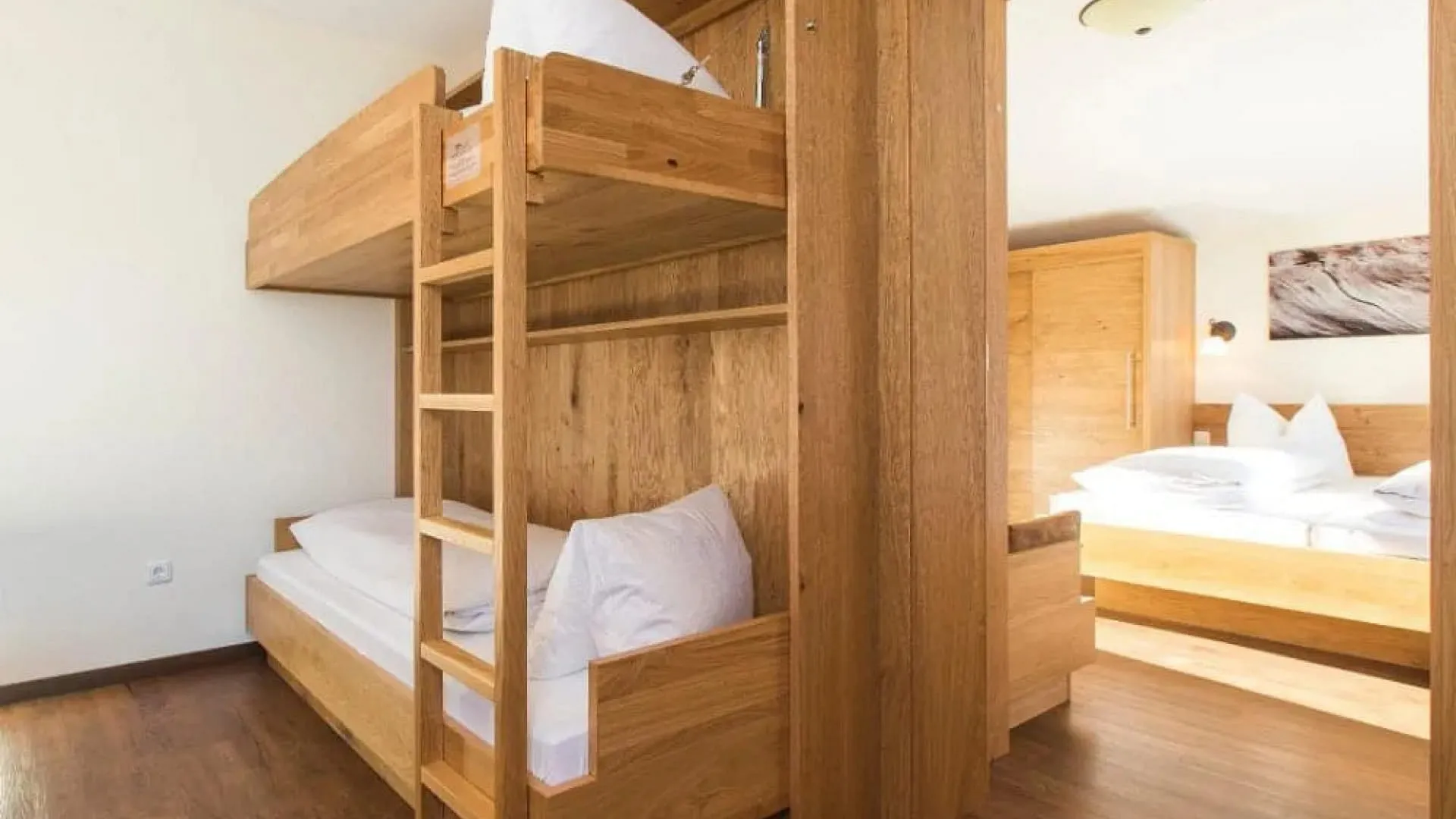 Helles Zimmer mit Doppelbett und Etagenbett aus Holz.