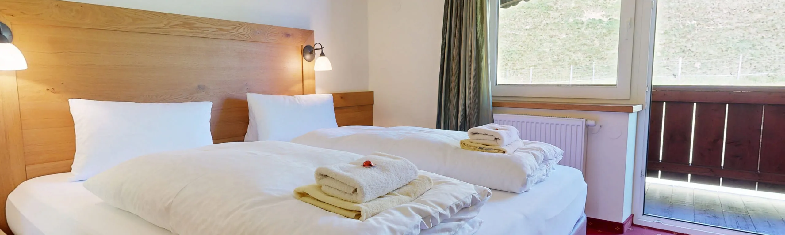 Helles Schlafzimmer mit Doppelbett, Handtüchern und Sofa im Hohe Tauern Hotel.
