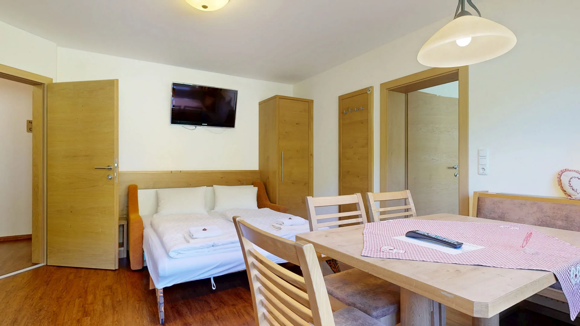 Wohnbereich mit Tisch, Stühlen und Schlafsofa, Fernseher an der Wand