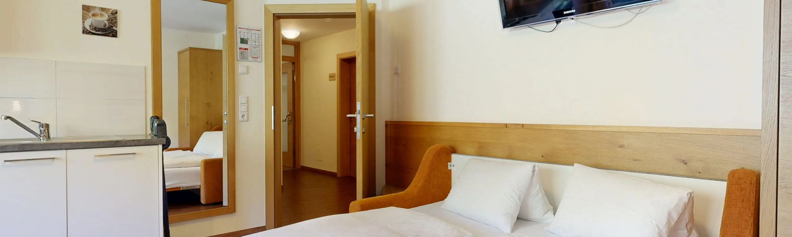 Einblick in ein Zimmer mit Bett, Fernseher und Küche.