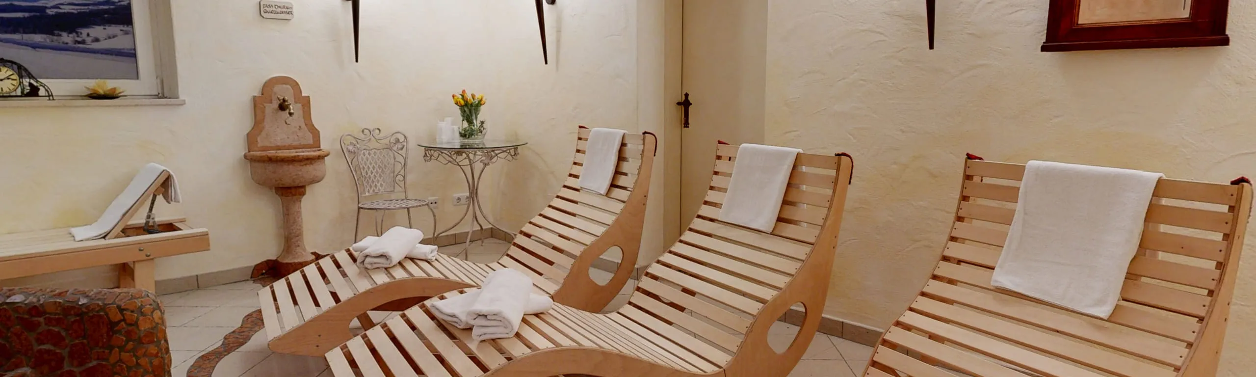 Holzliegestühle in einem Wellnessbereich mit Pflanze und Brunnen