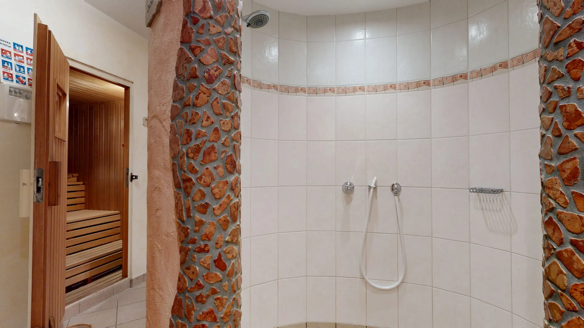 Sauna-Dusche mit gefliesten Wänden und separatem Saunabereich im Hintergrund